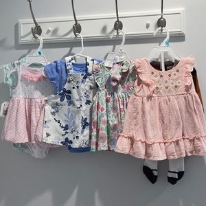 BRAND NEW 6 month old outfits. 4 dresses, 1 onsie, and one outfit.